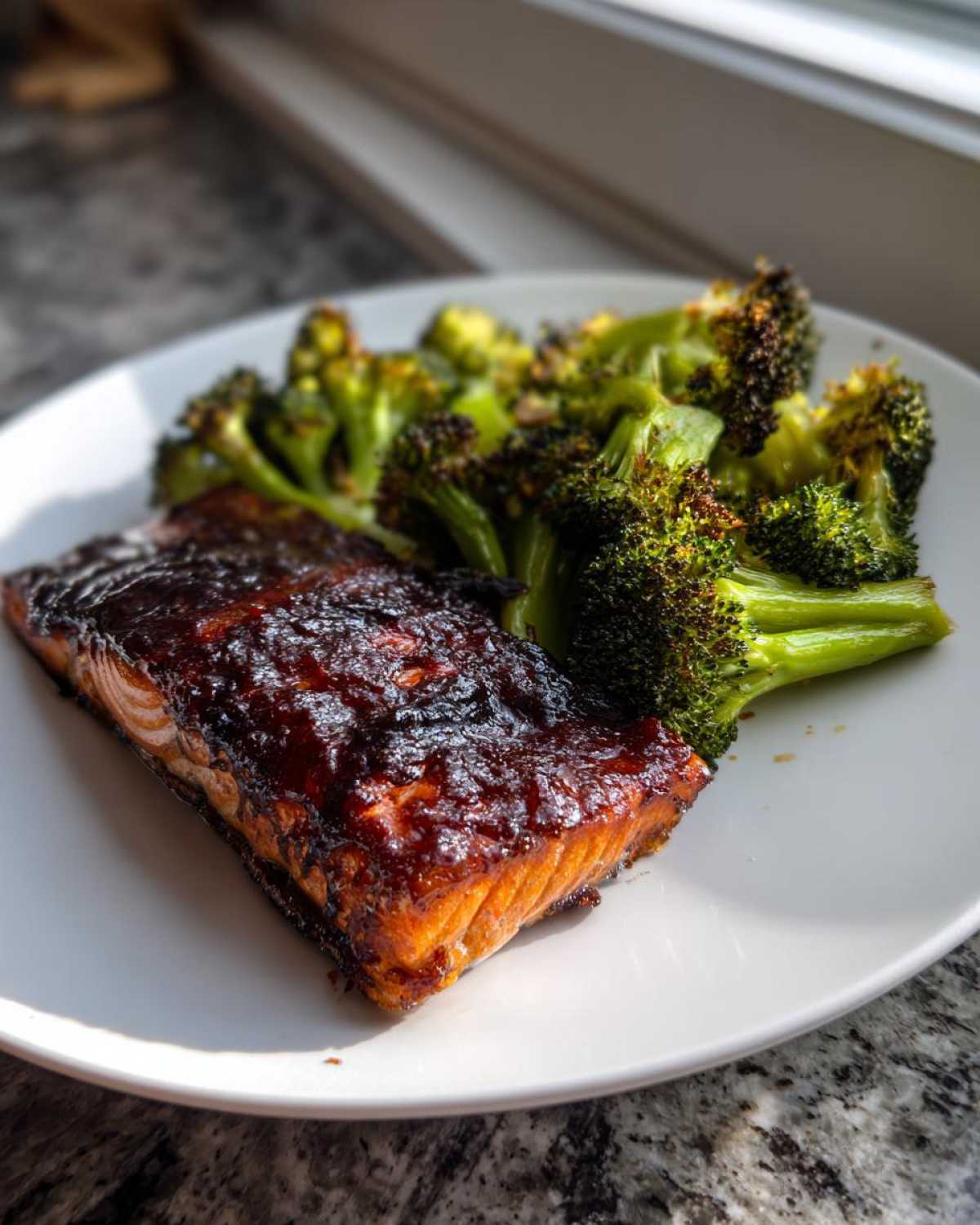A perfectly cooked fillet of Sheet Pan Honey Harissa Salmon with a dark, shiny glaze next to roasted broccoli florets.