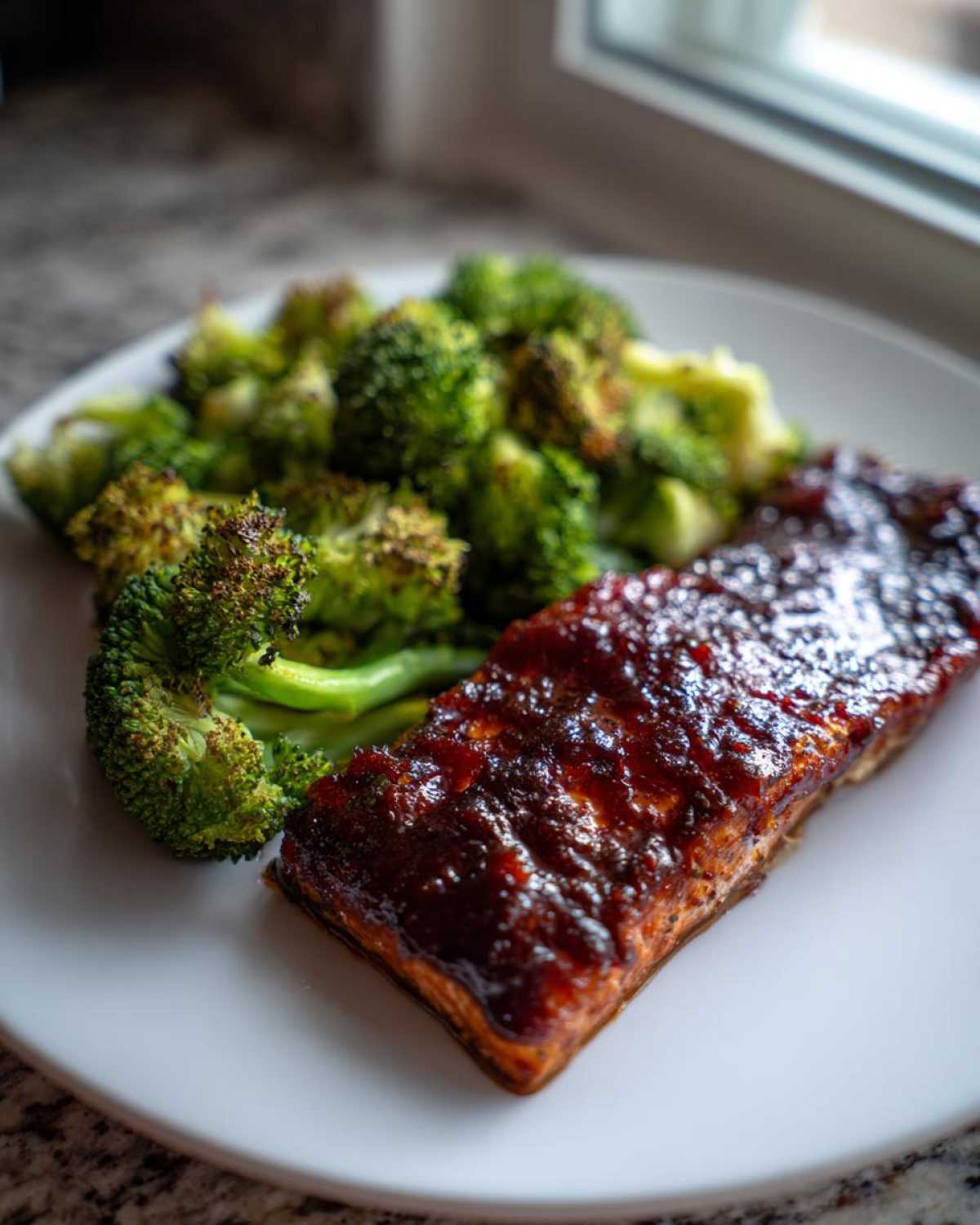 A serving of Sheet Pan Honey Harissa Salmon with a thick, glossy glaze next to roasted broccoli florets on a white plate.