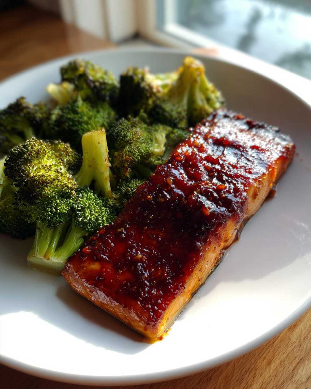 A perfectly cooked fillet of Sheet Pan Honey Harissa Salmon topped with a glossy, dark red glaze, served next to bright green roasted broccoli florets.