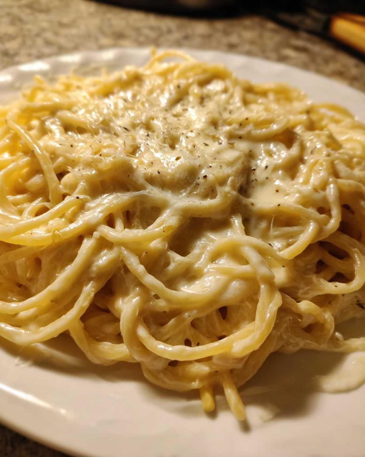 Close-up of spaghetti noodles generously coated in creamy Easy Cottage Cheese Alfredo Sauce and topped with pepper.