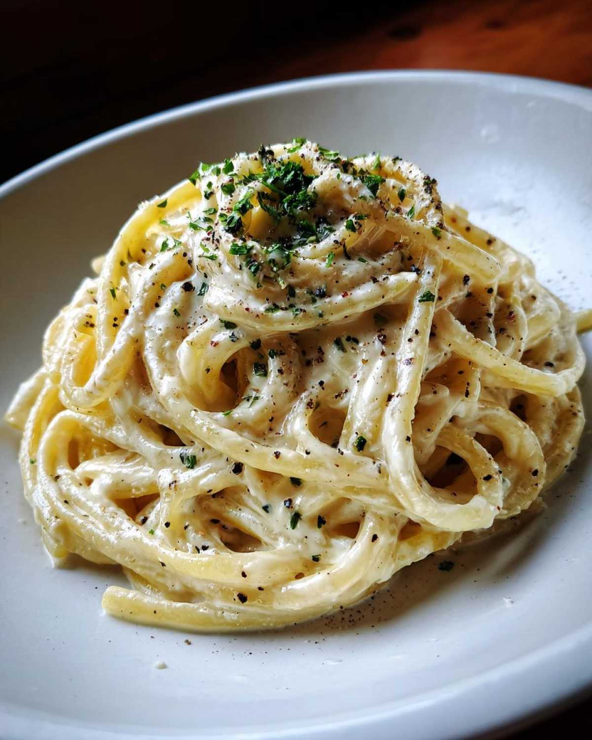 Close-up of spaghetti coated in a rich, white cream sauce, topped with black pepper and parsley.