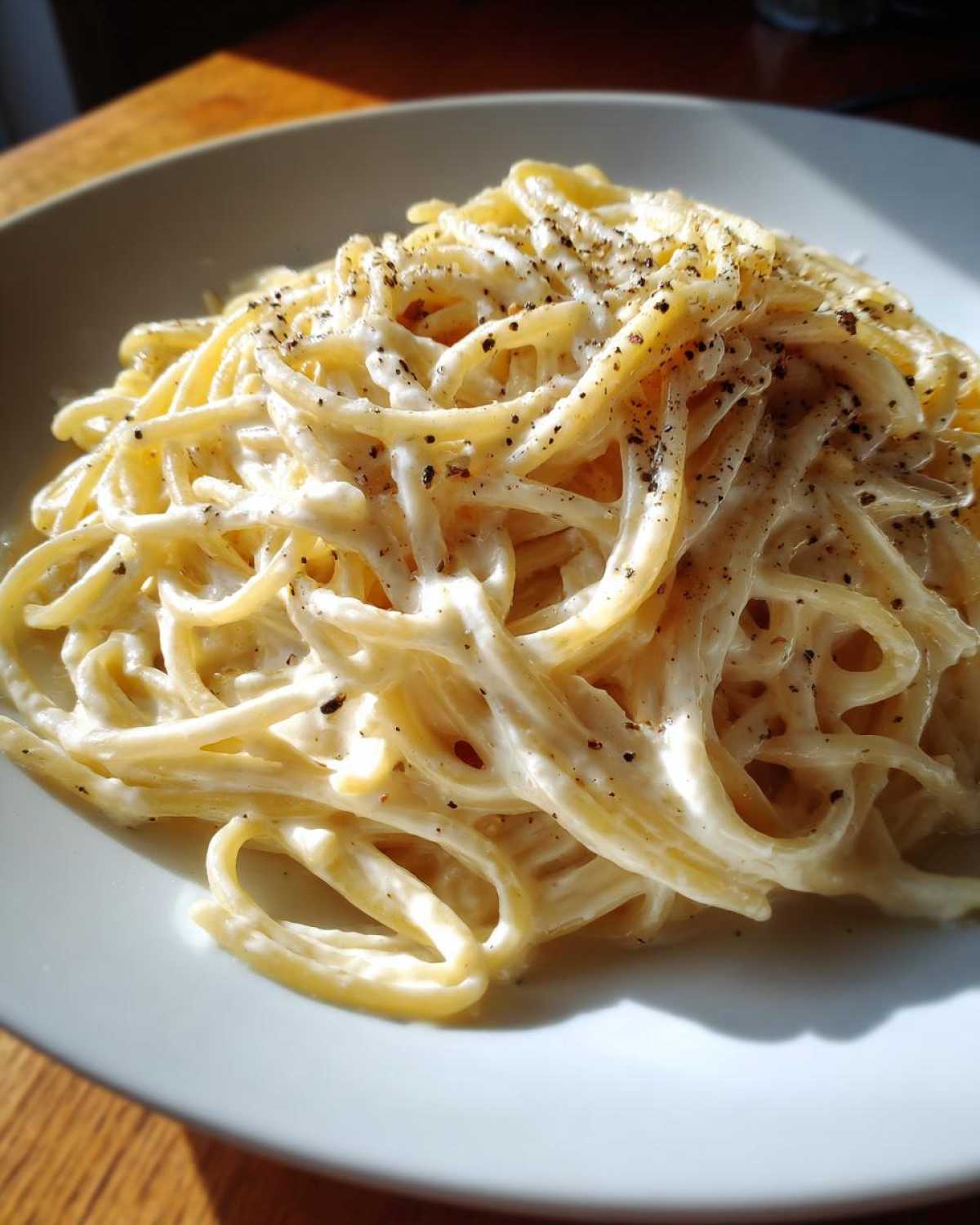 Close-up of spaghetti tossed in a rich, white cream sauce and heavily seasoned with black pepper.