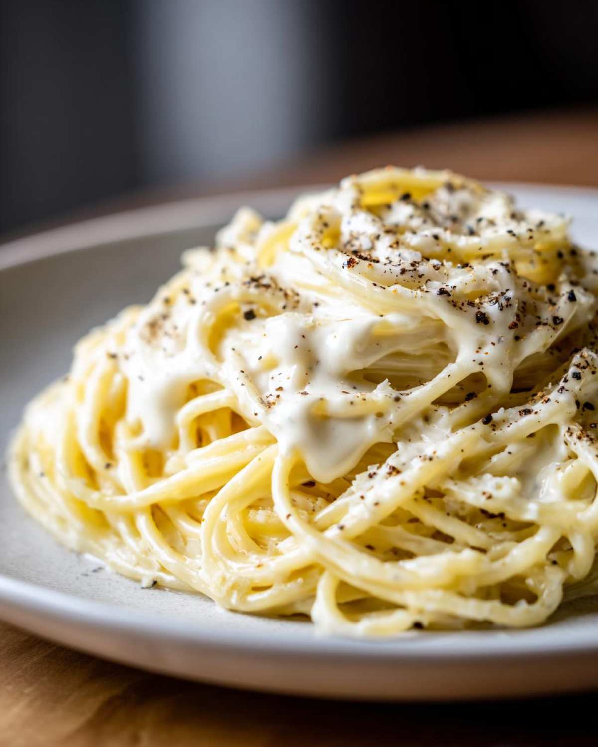 A close-up of spaghetti generously coated in a rich, white cream sauce and topped with cracked black pepper.