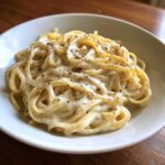 Close-up of spaghetti tossed in a rich, white cream sauce and topped with freshly cracked black pepper.