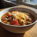 Close-up of a steaming white bowl filled with stuffed pepper soup, topped with melted cheese and rice.