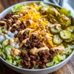 A close-up of a big mac salad featuring seasoned ground beef, shredded cheddar, pickles, onions, and special sauce over lettuce.