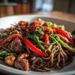 Close-up of a bowl of dark, saucy thai drunken noodles mixed with bright red bell peppers and green vegetables.