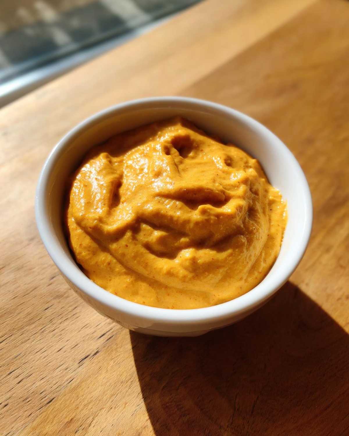 A small white bowl filled with thick, vibrant orange cheese sauce, sitting on a wooden surface.