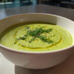A white bowl filled with bright green Vegan Creamy Cucumber Dill Soup, garnished with fresh dill and olive oil.