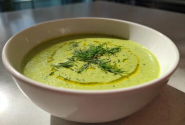 A white bowl filled with bright green Vegan Creamy Cucumber Dill Soup, garnished with fresh dill and olive oil.