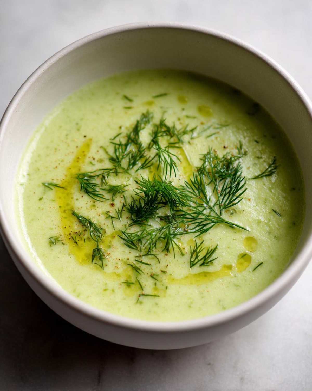 A close-up of Vegan Creamy Cucumber Dill Soup, topped with fresh dill and olive oil.