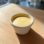A small white ramekin filled with thick, creamy Vegan Creamy Lemon Tahini Dressing, sitting on a light wooden surface.