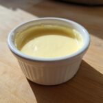 Close-up of smooth, pale yellow Vegan Creamy Lemon Tahini Dressing in a small white ramekin.
