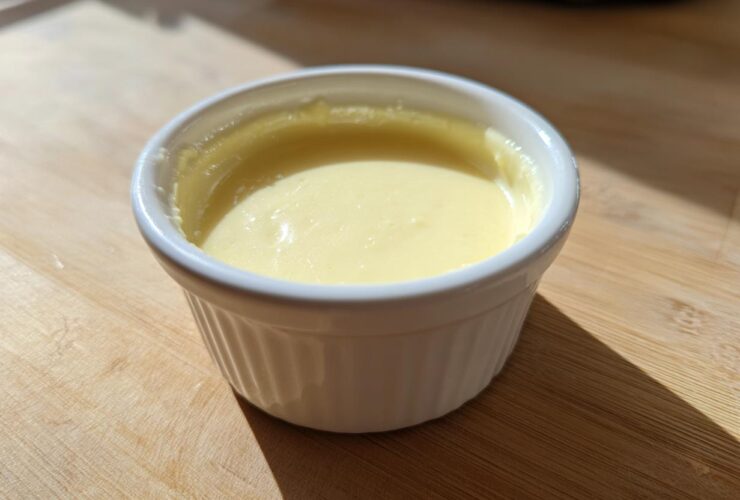 Close-up of smooth, pale yellow Vegan Creamy Lemon Tahini Dressing in a small white ramekin.