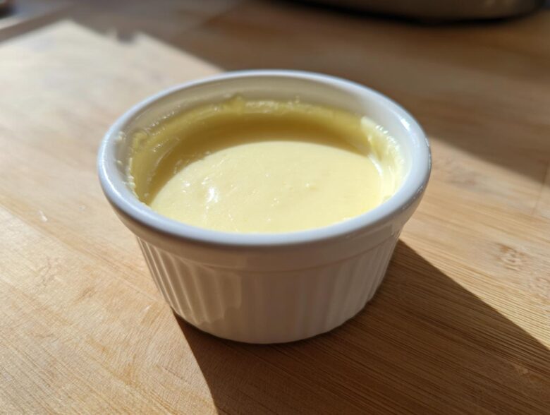 Close-up of smooth, pale yellow Vegan Creamy Lemon Tahini Dressing in a small white ramekin.