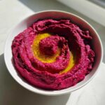 A vibrant bowl of Vegan Creamy Roasted Beet Hummus, swirled and topped with olive oil.