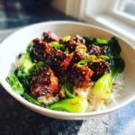 A close-up of a Vegan Crispy Sesame Tempeh Bowl featuring glazed tempeh cubes over white rice and bok choy.