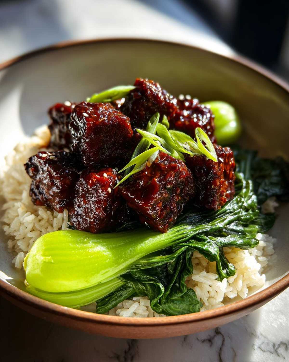 Close-up of a Vegan Crispy Sesame Tempeh Bowl featuring glazed tempeh cubes, steamed bok choy, and white rice, garnished with green onions.