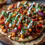 Close-up of Vegan One-Pan Chickpea Shawarma served on charred flatbread with red onion, peppers, and a white tahini drizzle.