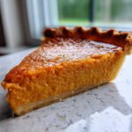 Close-up of a thick slice of velvety sweet potato pie showing the bright orange filling and fluted crust edge.
