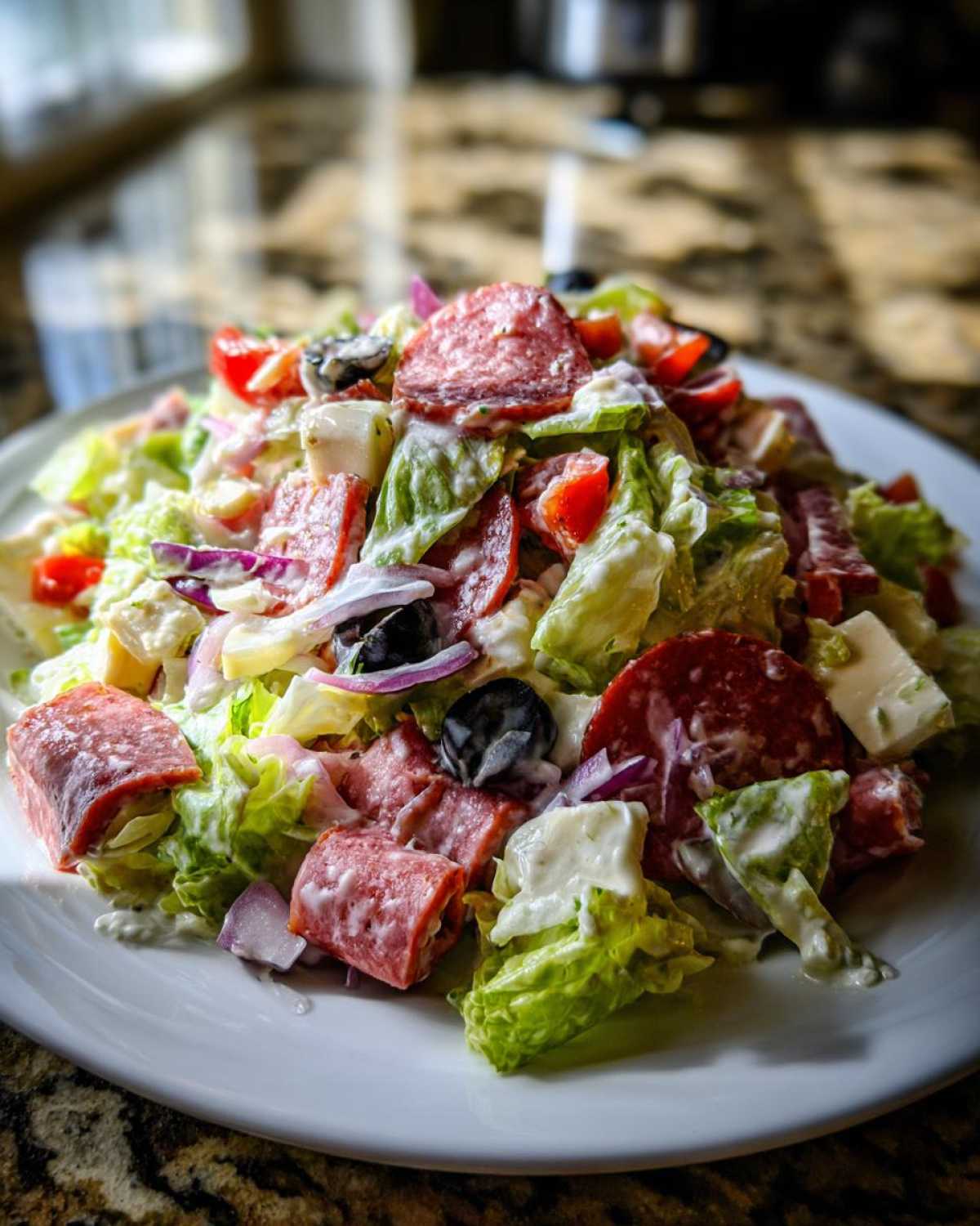 A vibrant, close-up view of a hearty grinder salad featuring lettuce, salami chunks, cheese cubes, red onion, and creamy dressing.